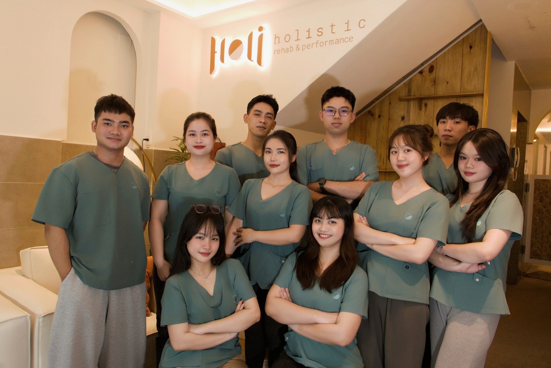 Đội ngũ HolisticVN trong đồng phục xanh, chụp trước bảng hiệu holistic rehab & performance
